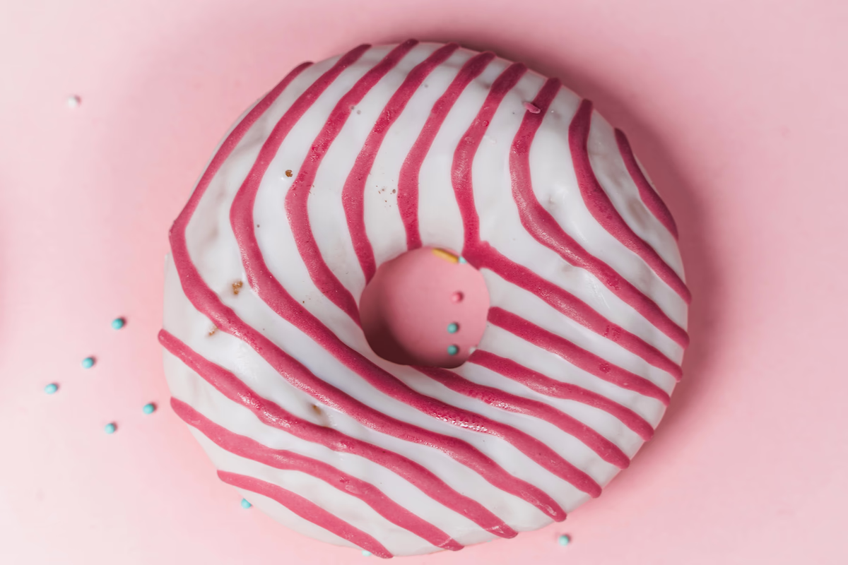 Vanilla frosted donut with red swirls on a pink background.
