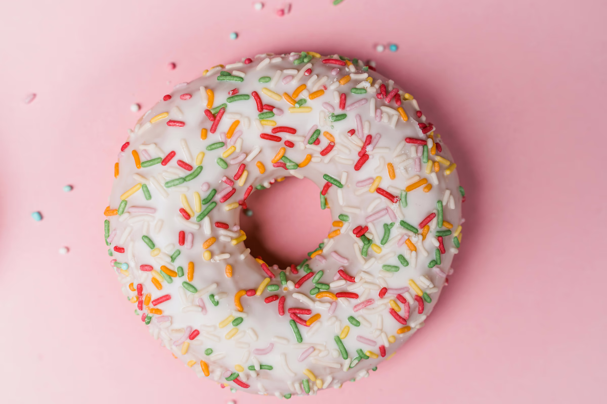 Vanilla frosted donut with sprinkles on a pink background.